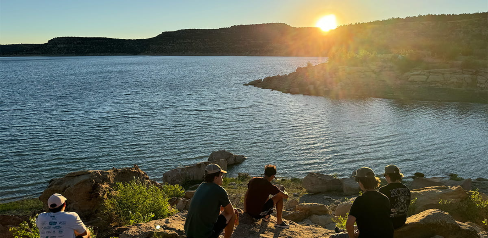 A group of young men sitting on the rocks at Navajo State Park watching the sunset.