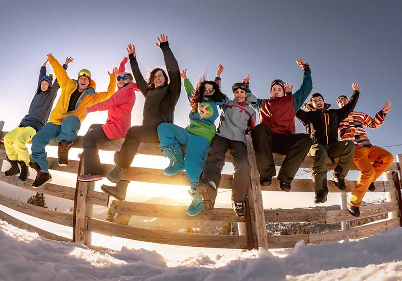 group of ski kids sitting on a fence as the sun sets